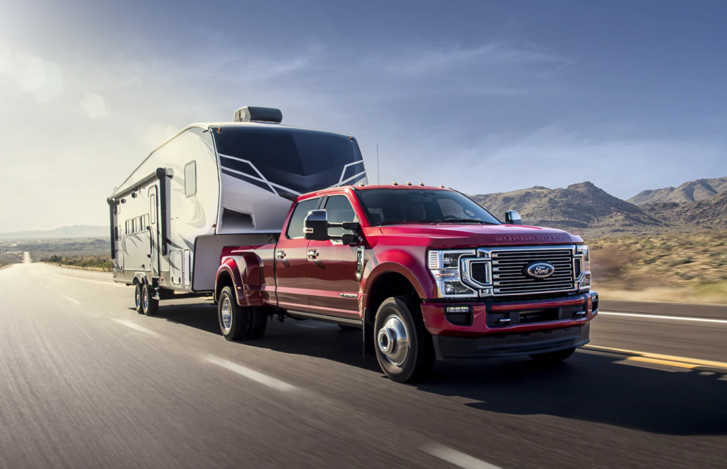 A red 2022 Ford F-350 towing a camper down a highway road.
