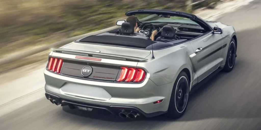 A convertible, silver Ford Mustang driving down a road.