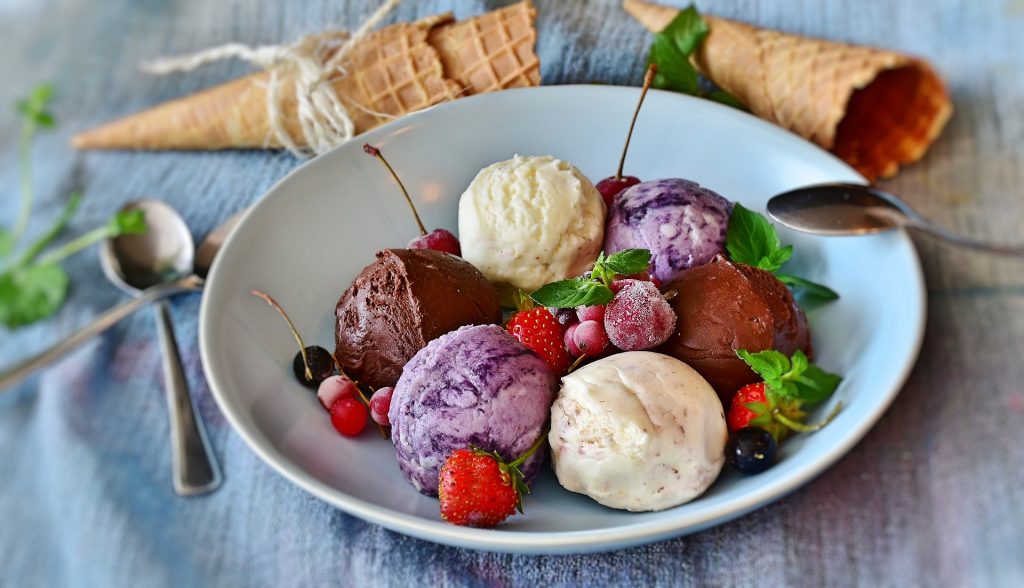 Different flavoured ice cream in a bowl with fruits and waffle cones surrounding it.