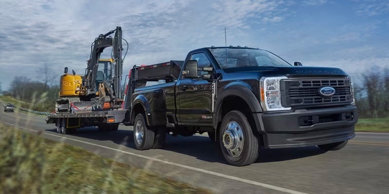 A black 2024 Ford F-250 towing a big machine.