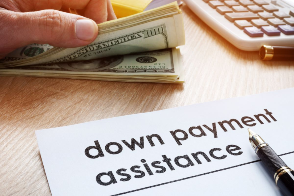 A person holding cash next to a document labeled "down payment assistance" with a pen and calculator.