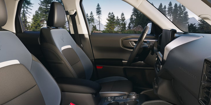 A close-up of the interior of a Ford Bronco SUV, showcasing the front seats, dashboard, and scenic outdoor view through the windows.