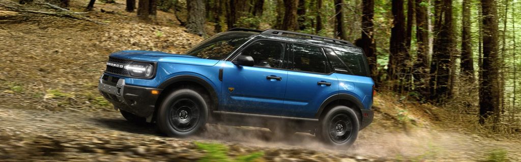 Blue Ford Bronco SUV driving through a forest trail off-road